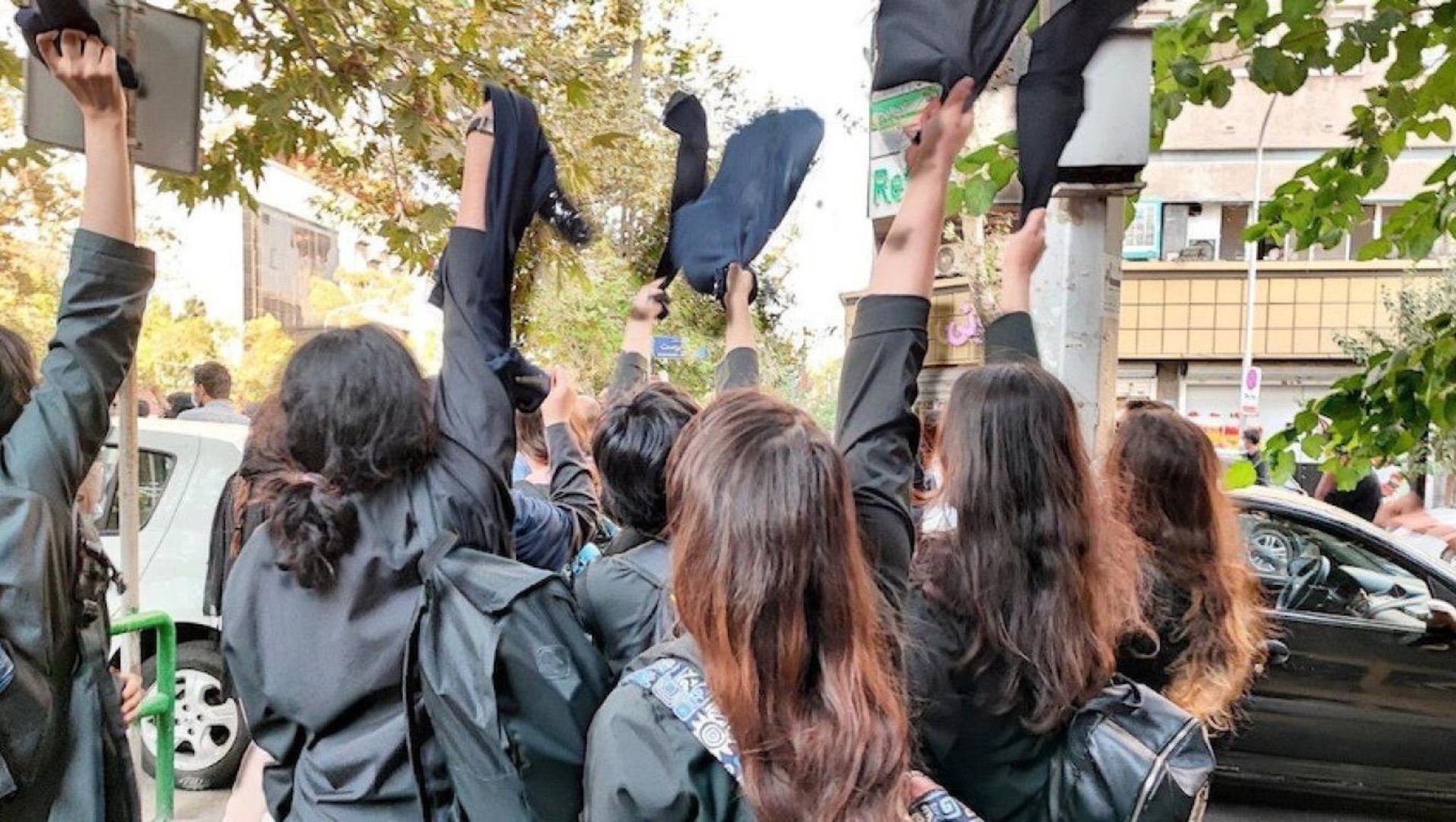 Das Bild zeigt mehrere junge Frauen von hinten, die schwarze Kopftücher in die Luft werfen