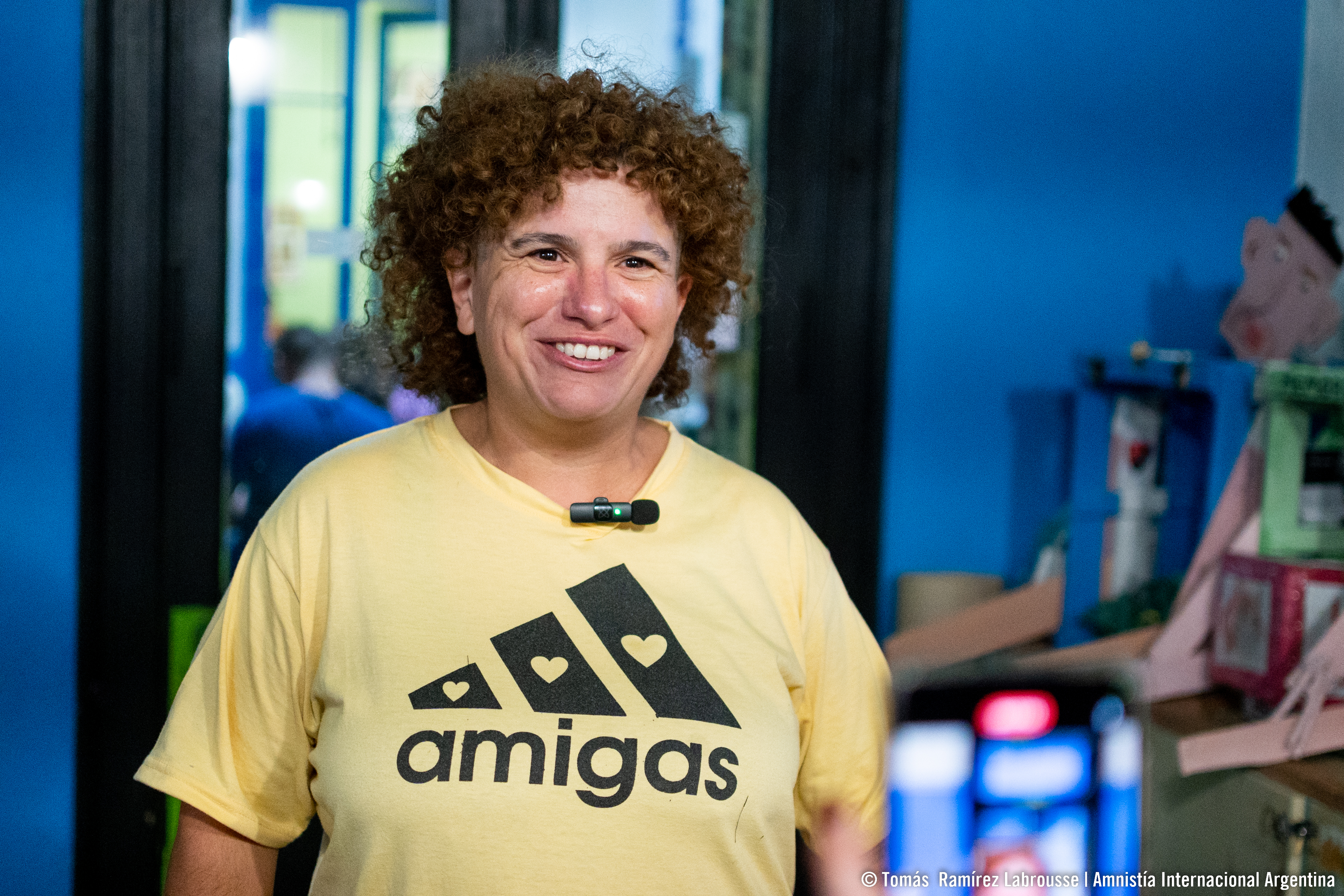 Das Bild zeigt das Porträtfoto einer lächelnden Frau. Sie trägt ein T-Shirt, auf dem steht: "Amigas".
