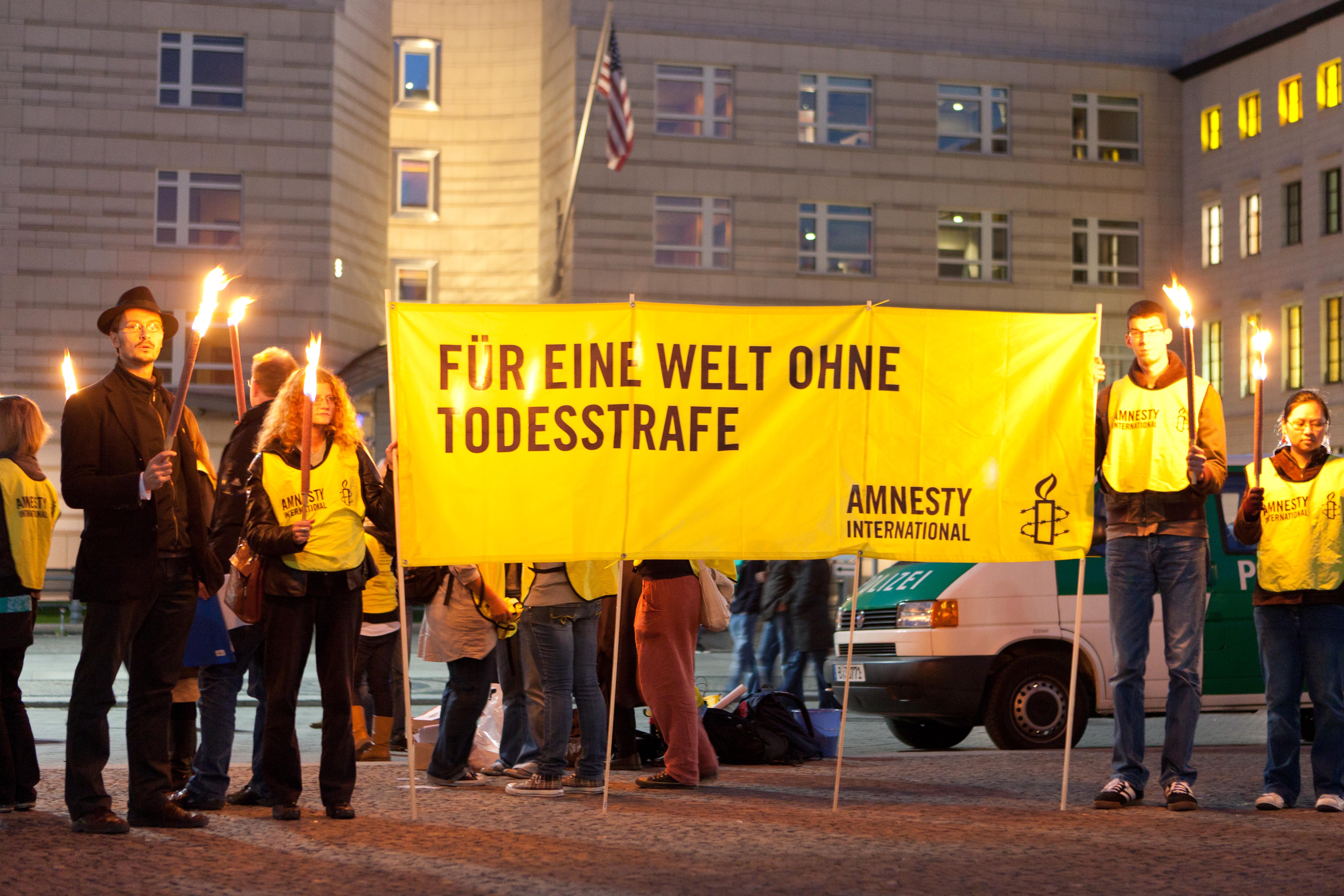 Mehrere Personen, die Fackel in den Händen halten, stehen neben einem Banner, auf dem steht: "Für eine Welt ohne Todesstrafe".