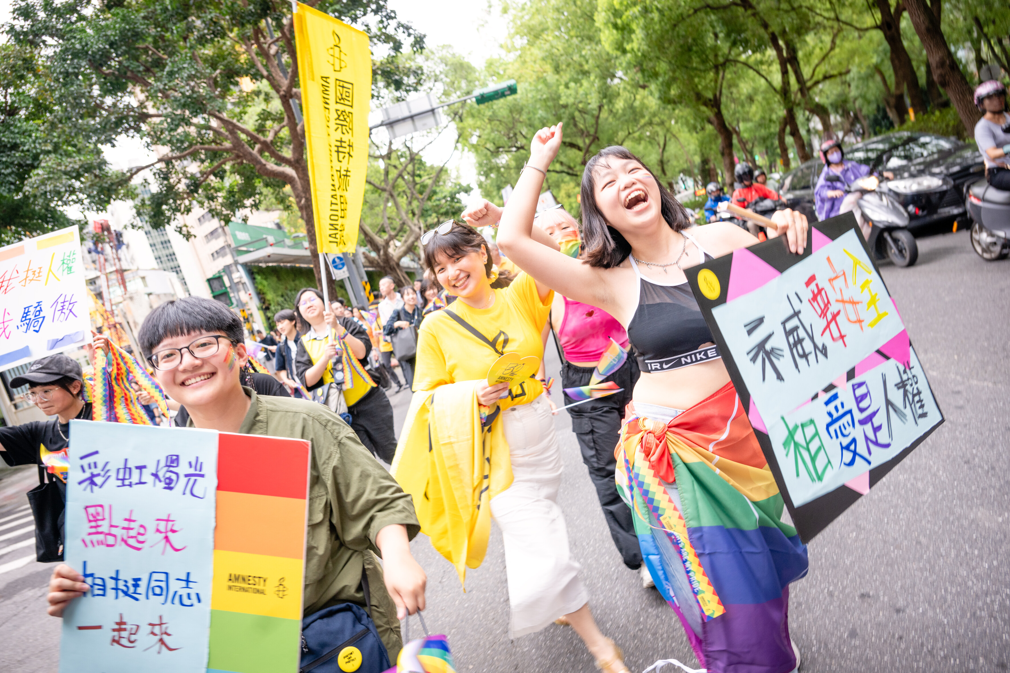 Das Foto zeigt mehrere fröhliche lachende Personen bei einer Demonstration, die Schider in der Hand halten. Im Hintergrund ragt eine große Fahne mit Amnesty-Logo aus der Menge.