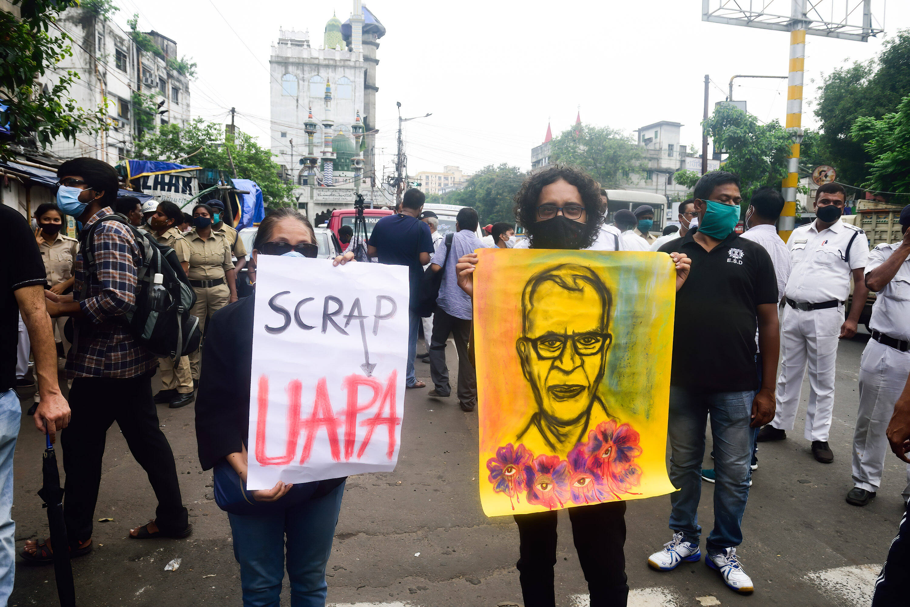 Das Foto zeigt eine Frau und eine Mann bei einer Demonstration. Die Frau hält ein Schild hoch, auf dem steht: "Scrap UAPA". Der Mann hält ein Zeichnung mit dem Gesicht von Stan Swamy hoch. 