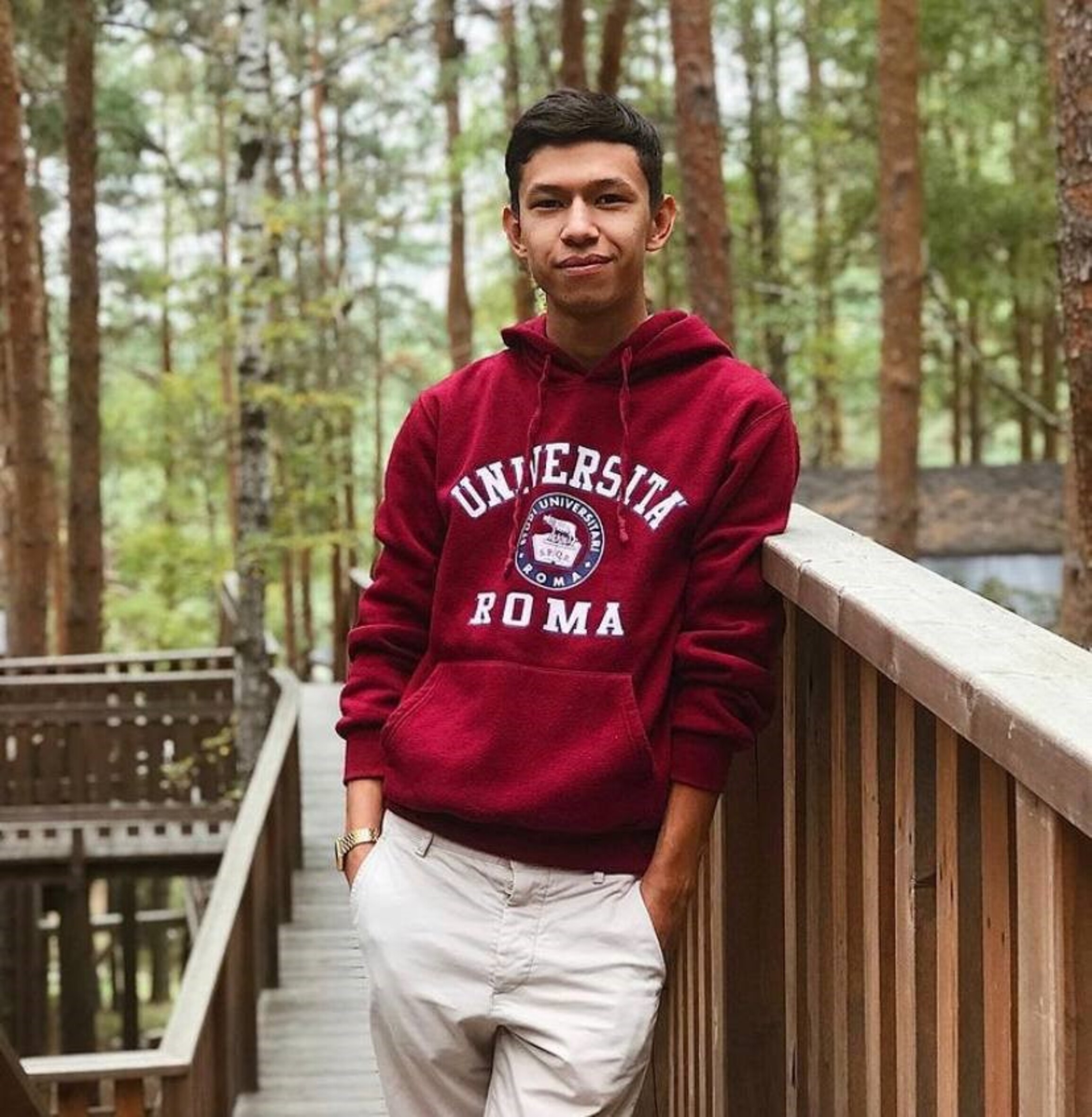 Das Foto zeigt Temirlan Ensebek, der einen Kapuzenpulli trägt und die Hände in die Hosentaschen gesteckt hat. Er lehnt an einem Geländer und lächelt in die Kamera.