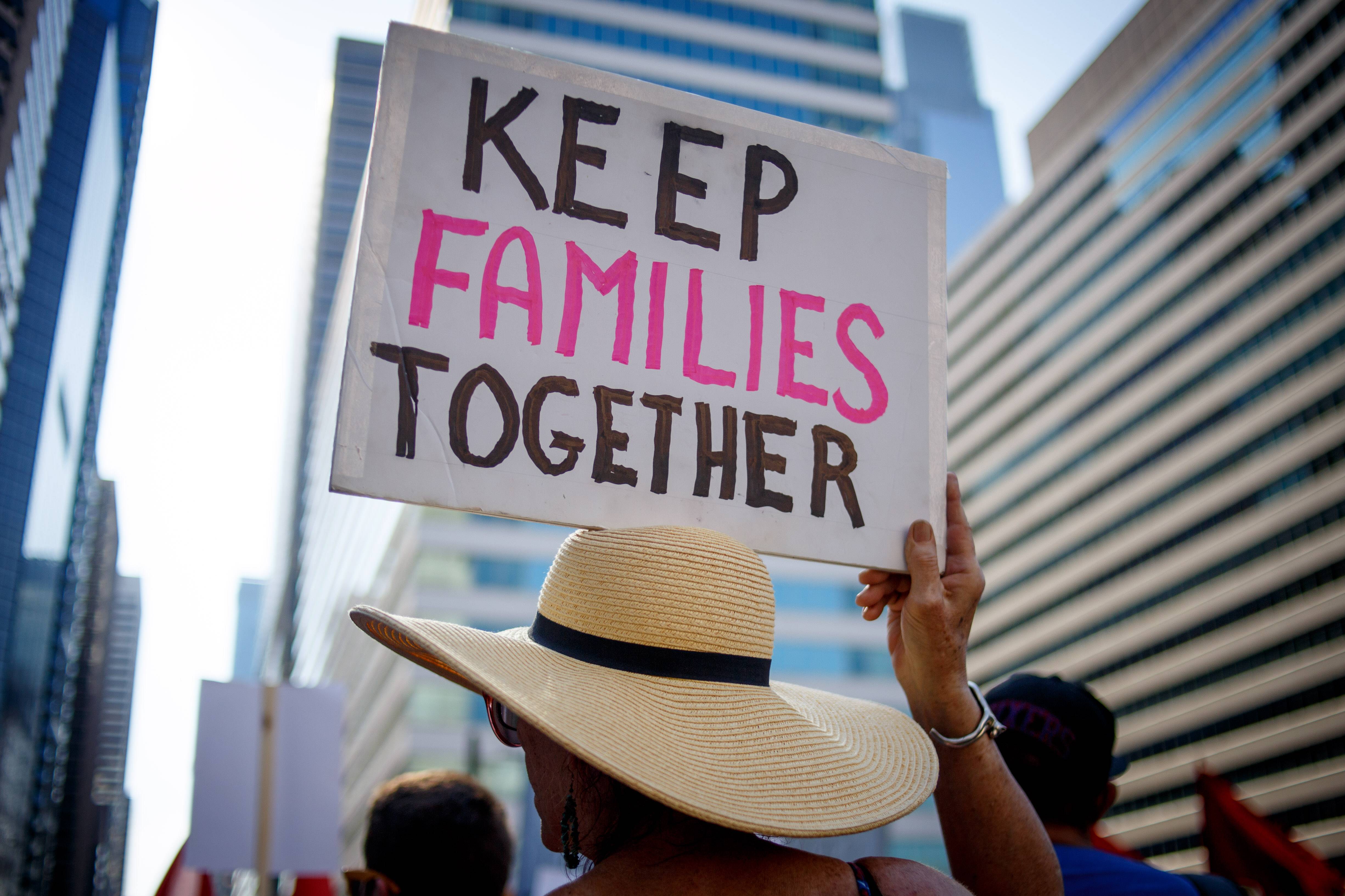 Eine Person hält bei einer Demonstration ein Plakat hoch, auf dem steht: "Keep families together".