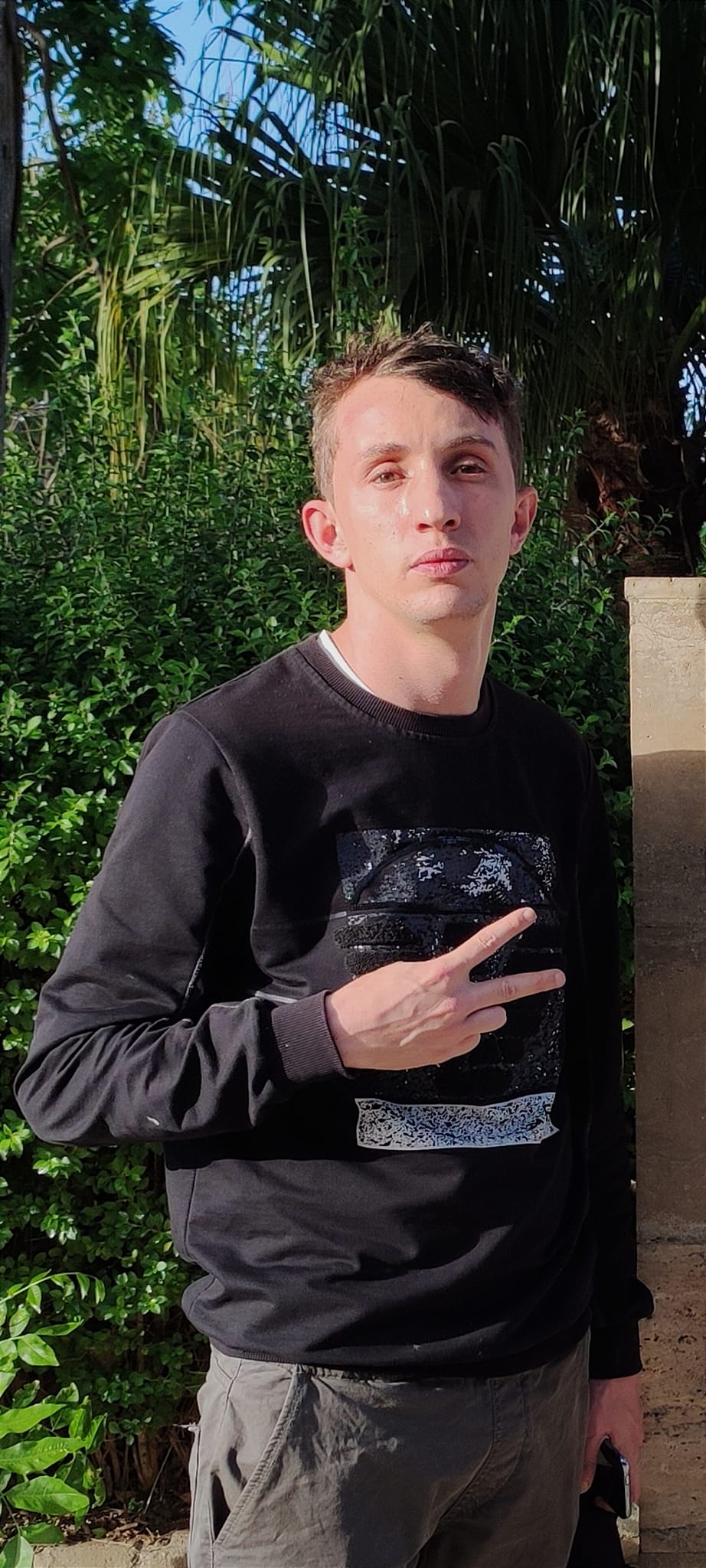 Das Foto zeit Mohamed Tadjadit vor einem Strauch und Bäumen. Er blick erst in die Kamera.