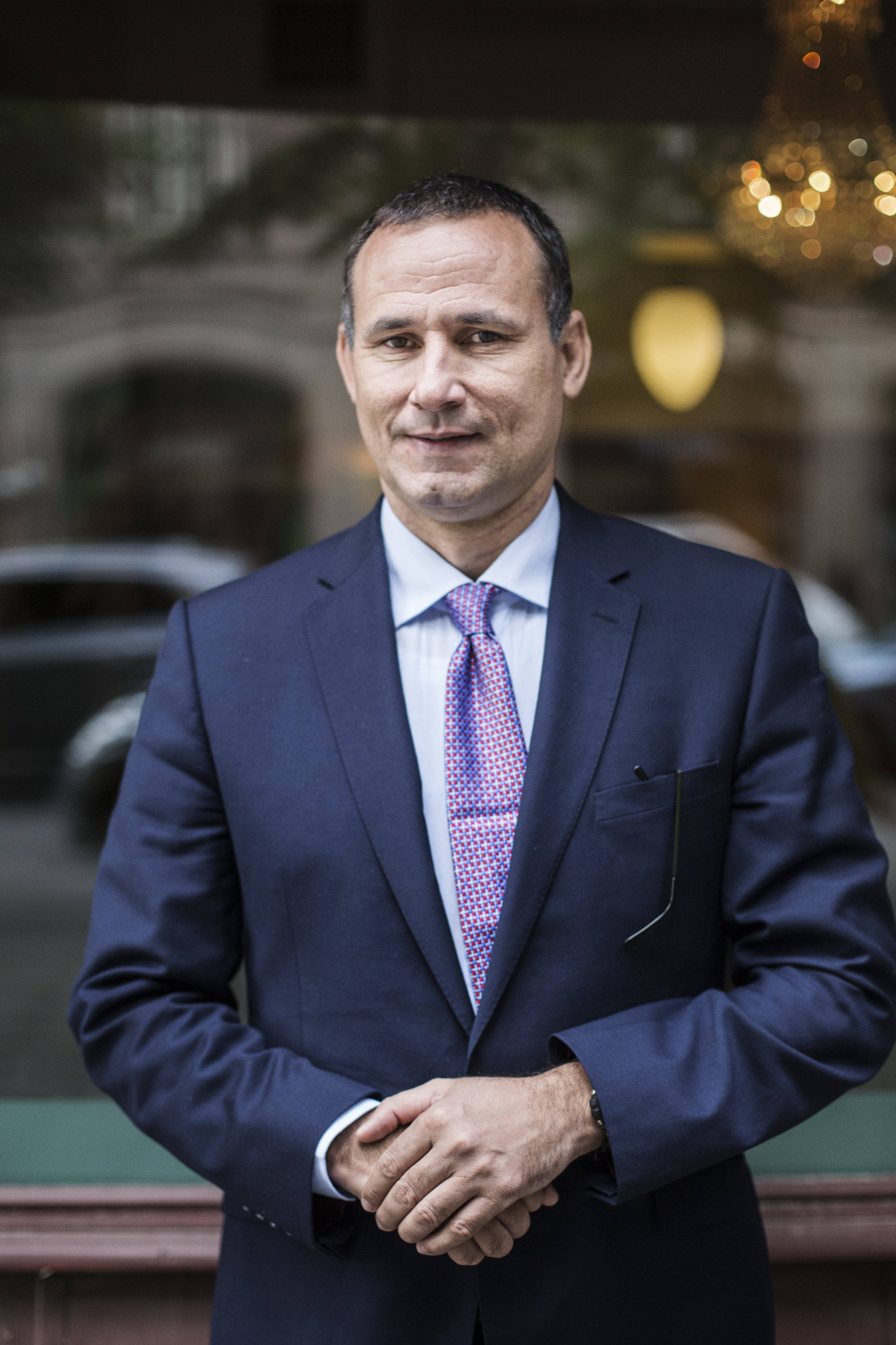 Das Foto zeigt José Daniel Ferrer vor einem Schaufenster stehend. Er trägt Anzug, Hemd und Krawatte und lächelt in die Kamera.
