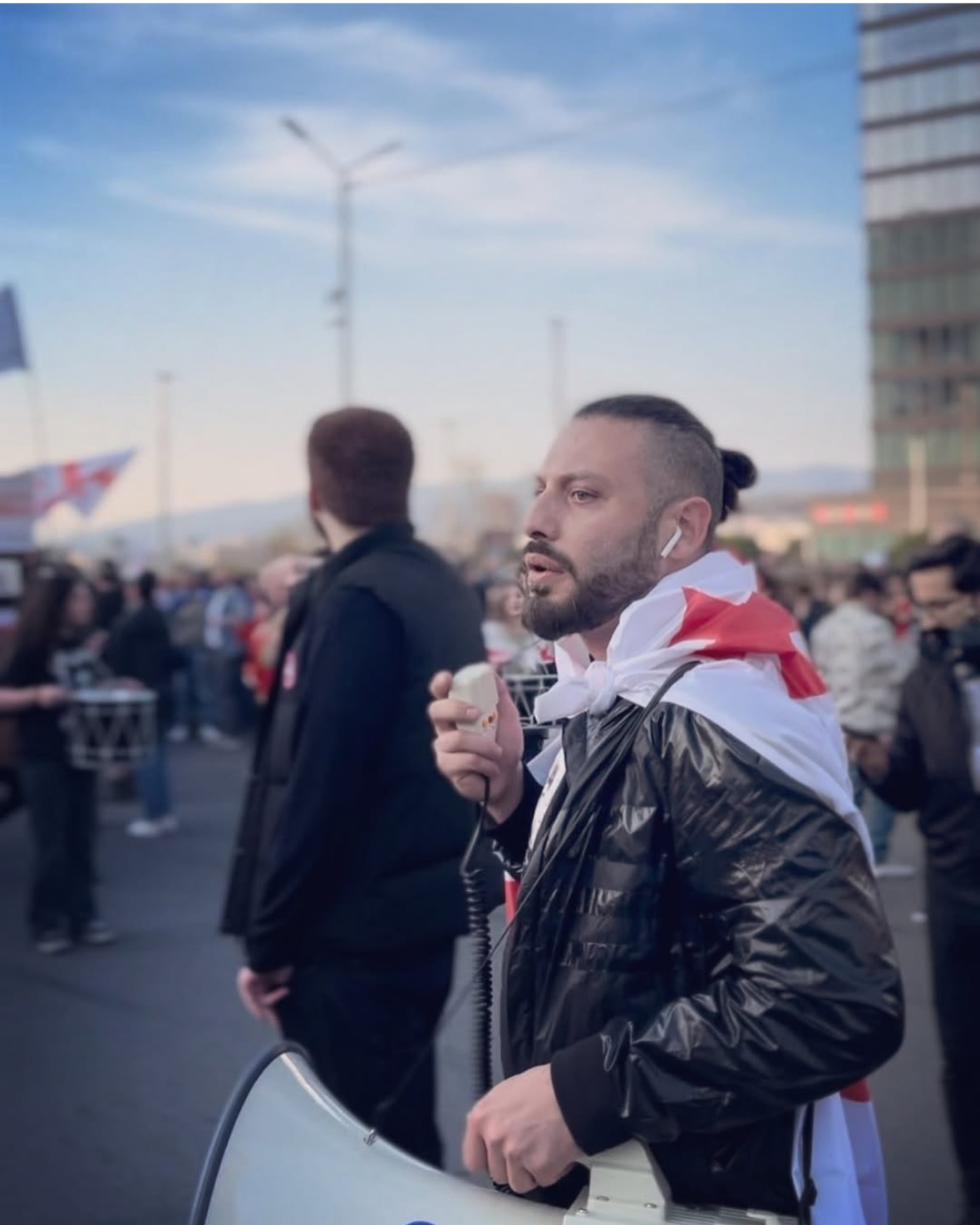 Ein Mann mit einer Flagge, die umgebunden hat. In der Hand hält er ein Megafon