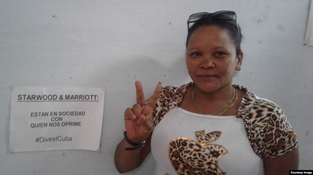 Das Foto zeigt Donaida Pérez Paseiro vor einer Wand stehend. Sie lächelt leicht und formt den Zeige- und den Mittelfinger der rechten Hand zum Victory-Zeichen.