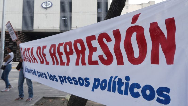 Das Foto zeigt Personen, die auf einem Platz ein großes Banner ausgebreitet haben, auf dem unter anderem steht: "Basta de repression".