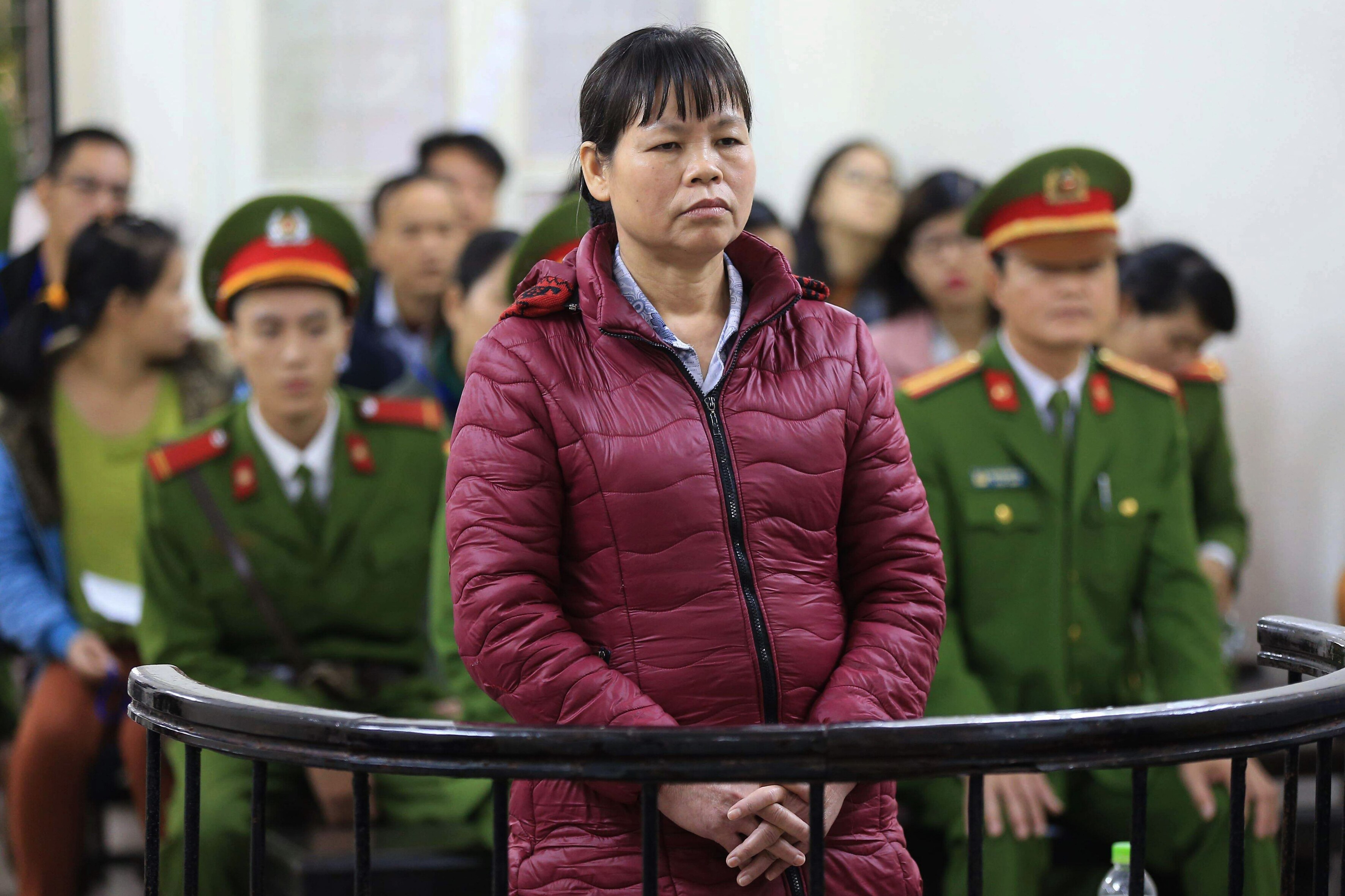Das Foto zeigt  Cấn Thị Thêu stehend in einem Gerichtssaal. Sie hat die Hände gefaltet und Blick nach vorne. Hinter ihr sitzen Beamte in Uniform und Publikum.