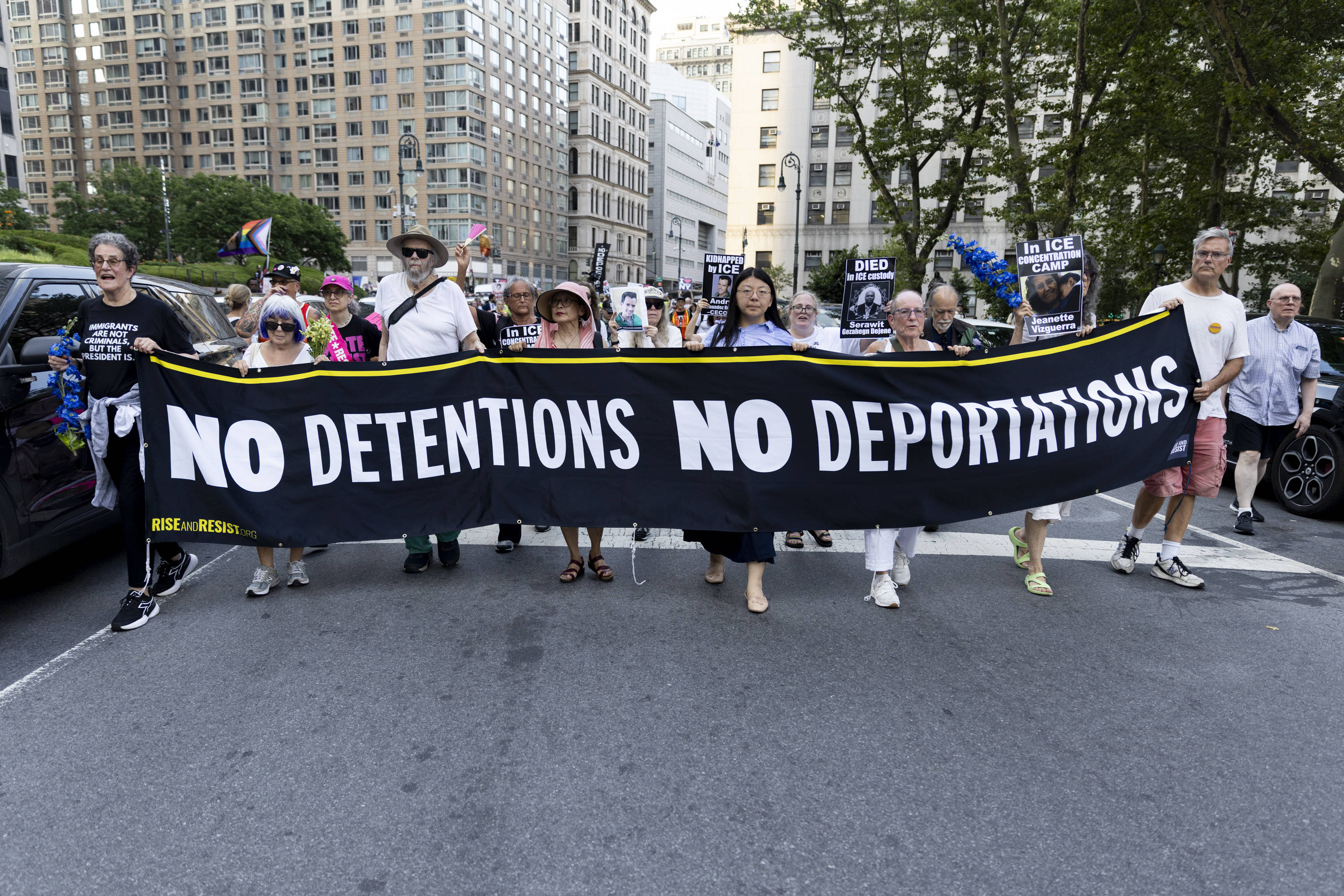 An der Spitze eines Demonstrationszuges, der durch die Straßen zieht, tragen mehrere Menschen ein Banner vor sich her, auf dem steht: "No Detentions! No Deportations!".
