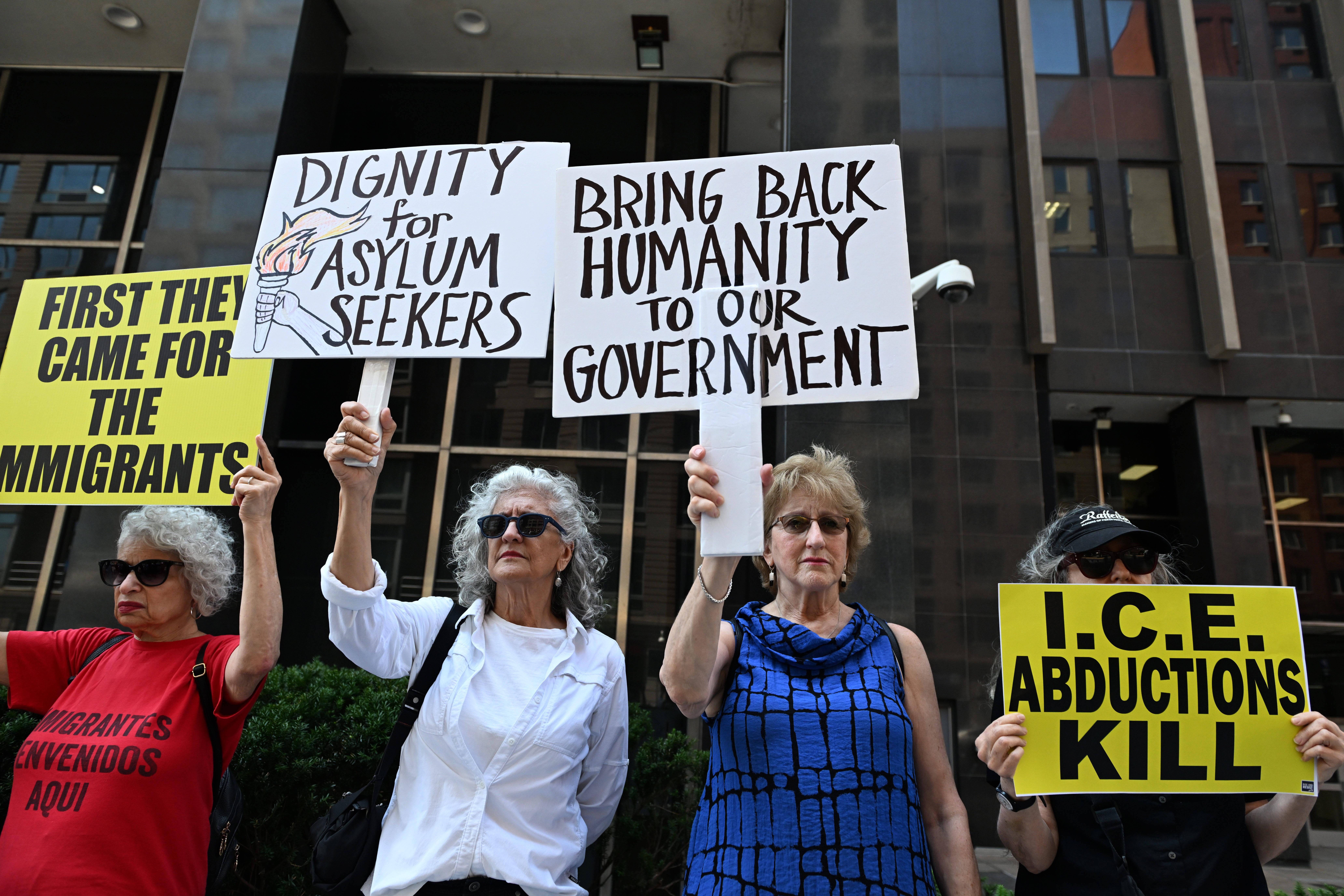Das Foto zeigt vier Frauen bei einer Protestaktion vor einem Gebäude. Sie halten Schilder hochm auf denen unter anderem steht: "Dignity for Asylum Seekers". Oder: "First they came for the immigrants".