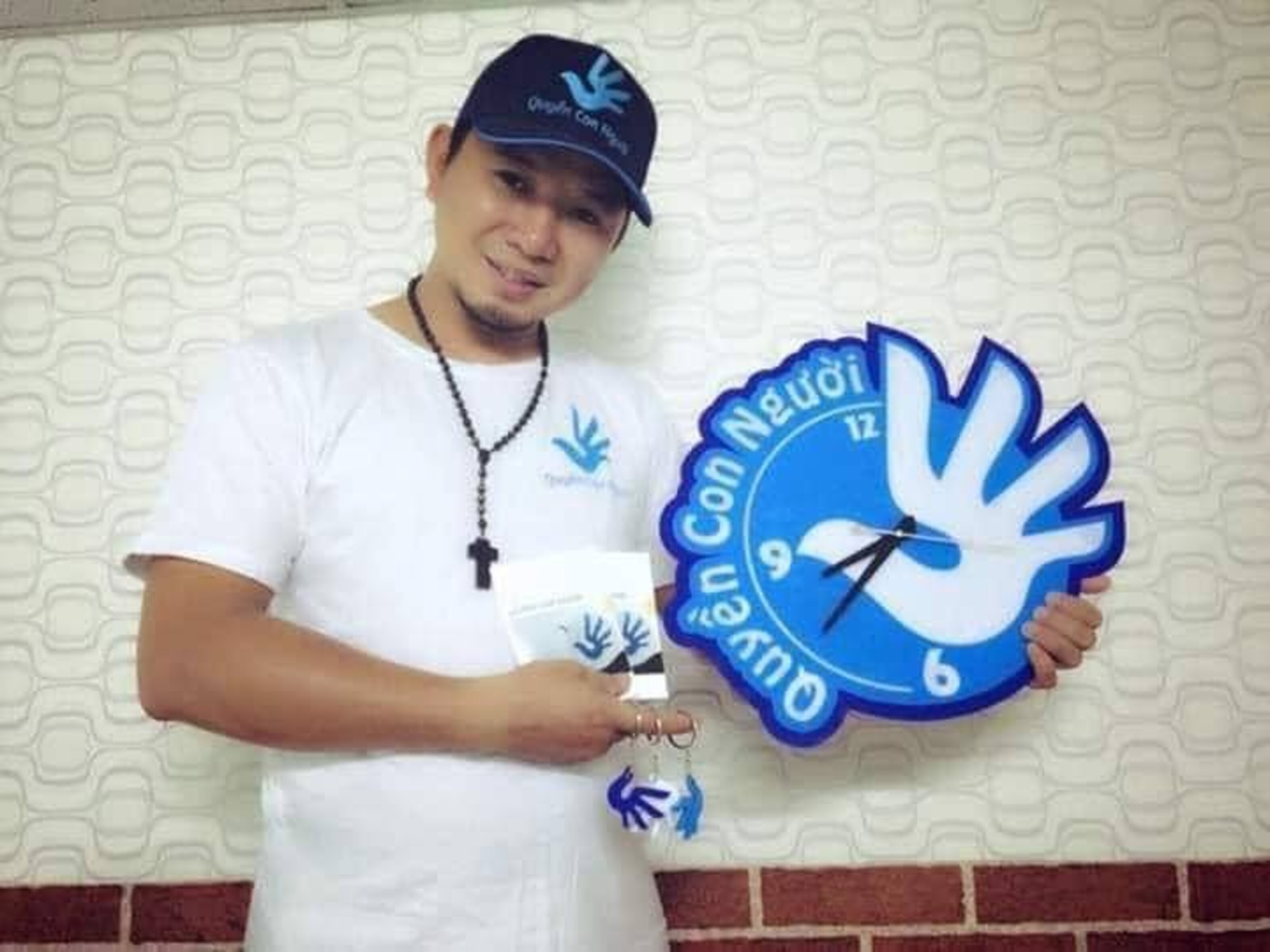 Das Foto zeigt Bùi Tuấn Lâm, der in seiner linken Hand eine große Uhr hält, auf die er mit seiner rechten Hand zeigt. Er trägt eine Baseballkappe und lächelt leicht in die Kamera.