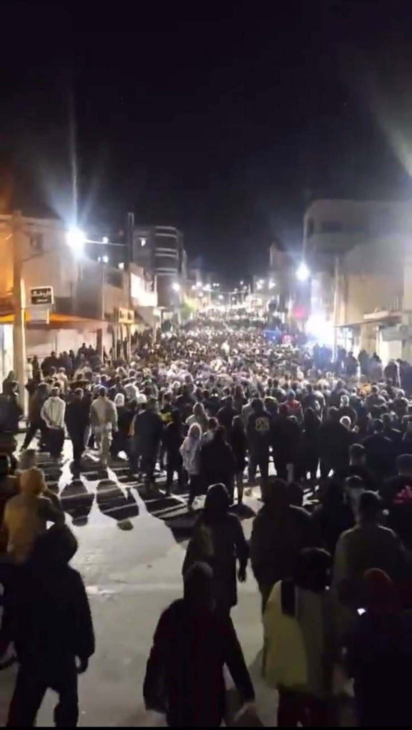 Das Foto zeigt einen großen Demonstrationszug, der nachts durch die beleuchtete Straße in einer Stadt zieht.
