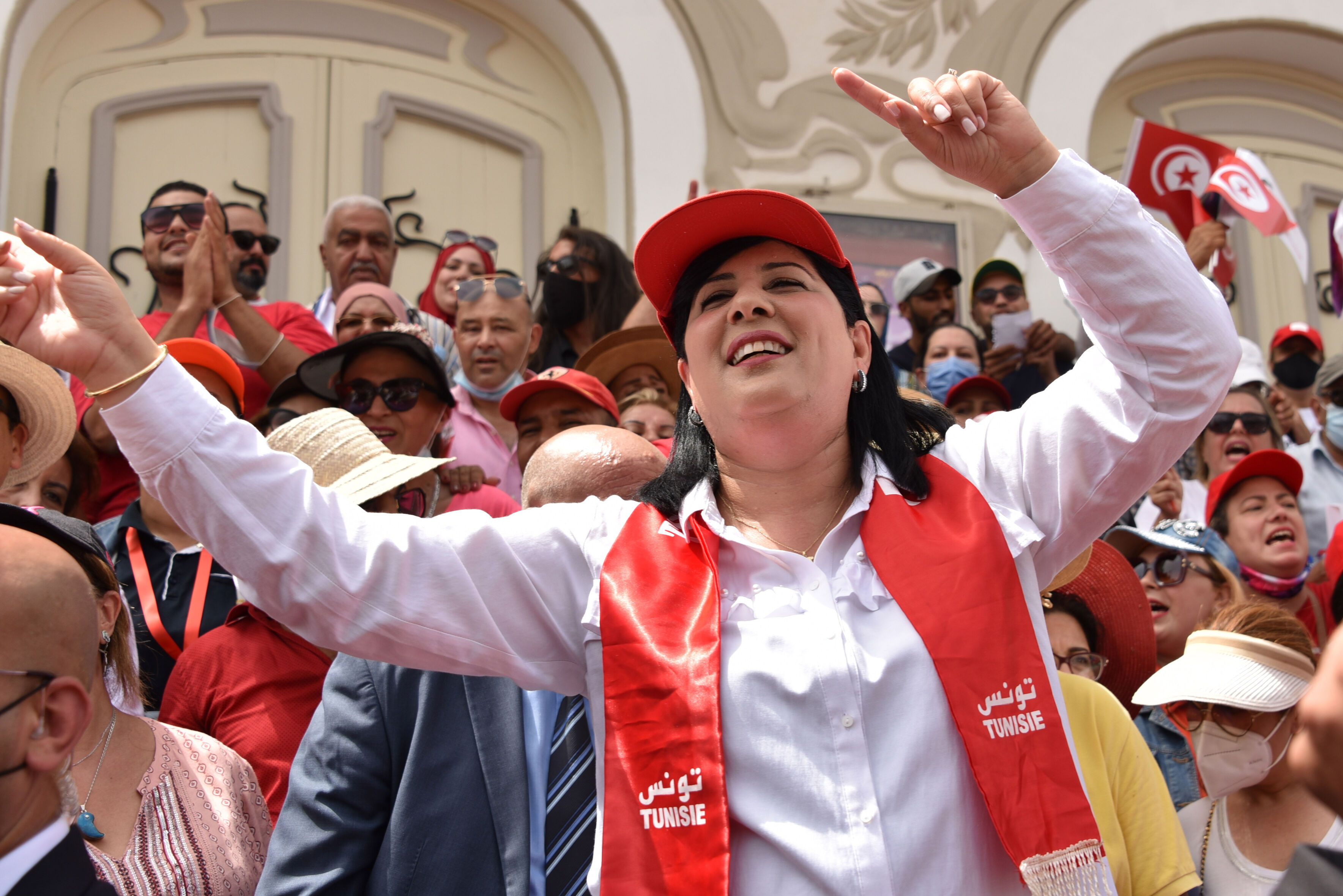Das Foto zeigt Abir Moussi inmitten einer Menschenmenge. Sie lacht und trägt eine Schirmmütze und einen Schal mit der Aufschirft "Tunisie".