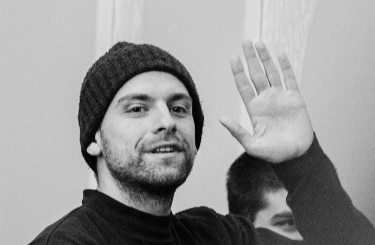 Das Foto zeigt Andro Chichinadze. Er trägt eine Strickmütze und lächelt und winkt mit seiner linken Hand.