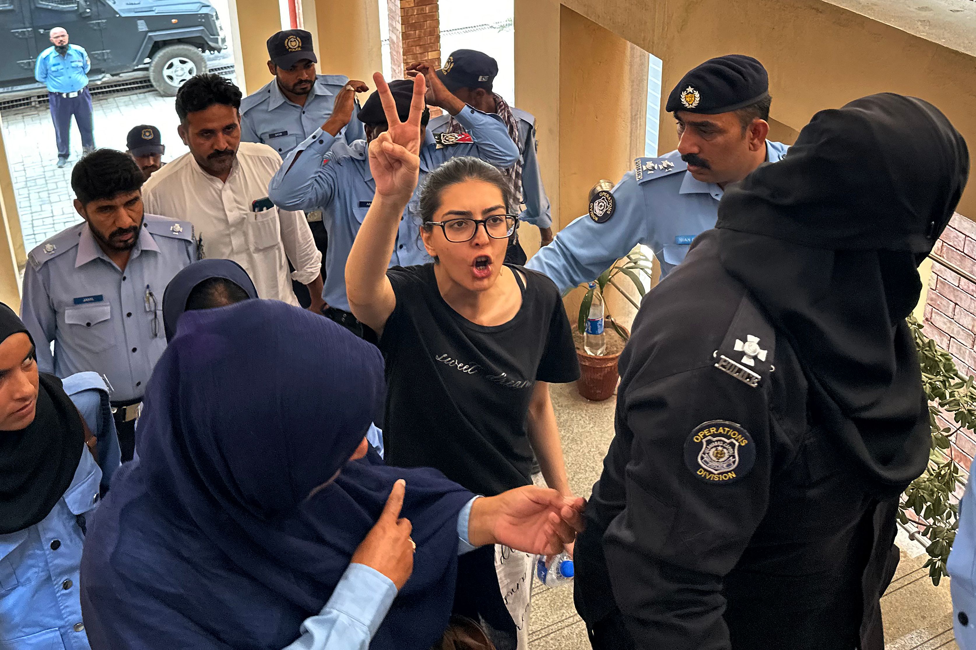 Eine Frau ist umringt von Polizeibeamten und -beamtinnen. Sie hebt die rechte Hand und macht das Victory-Zeichen