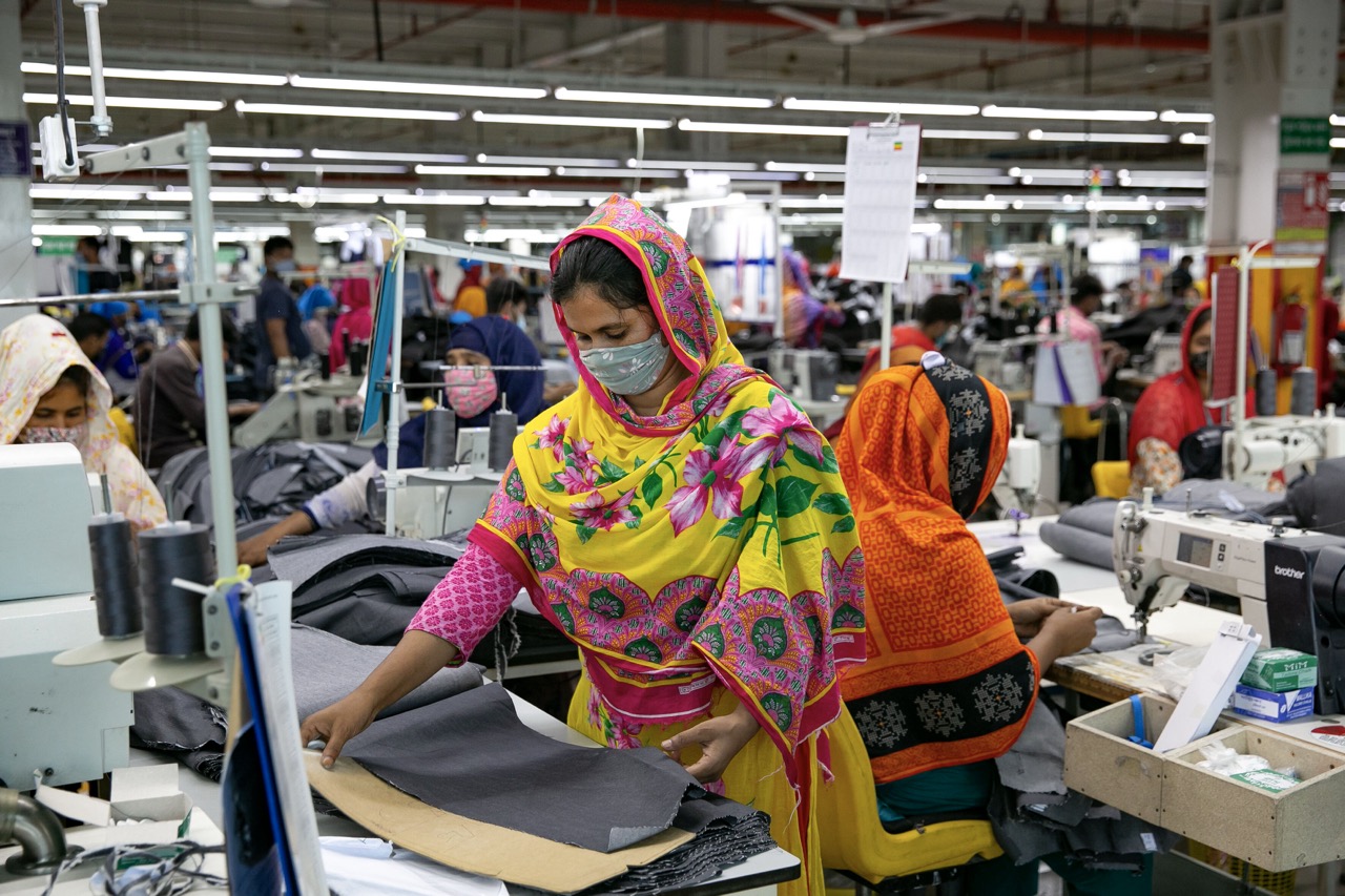 Das Foto zeigt mehrere Frauen mit Mundschutz, gekleidet in bunten Kleidern. Sie arbeiten an Nähmaschinen.