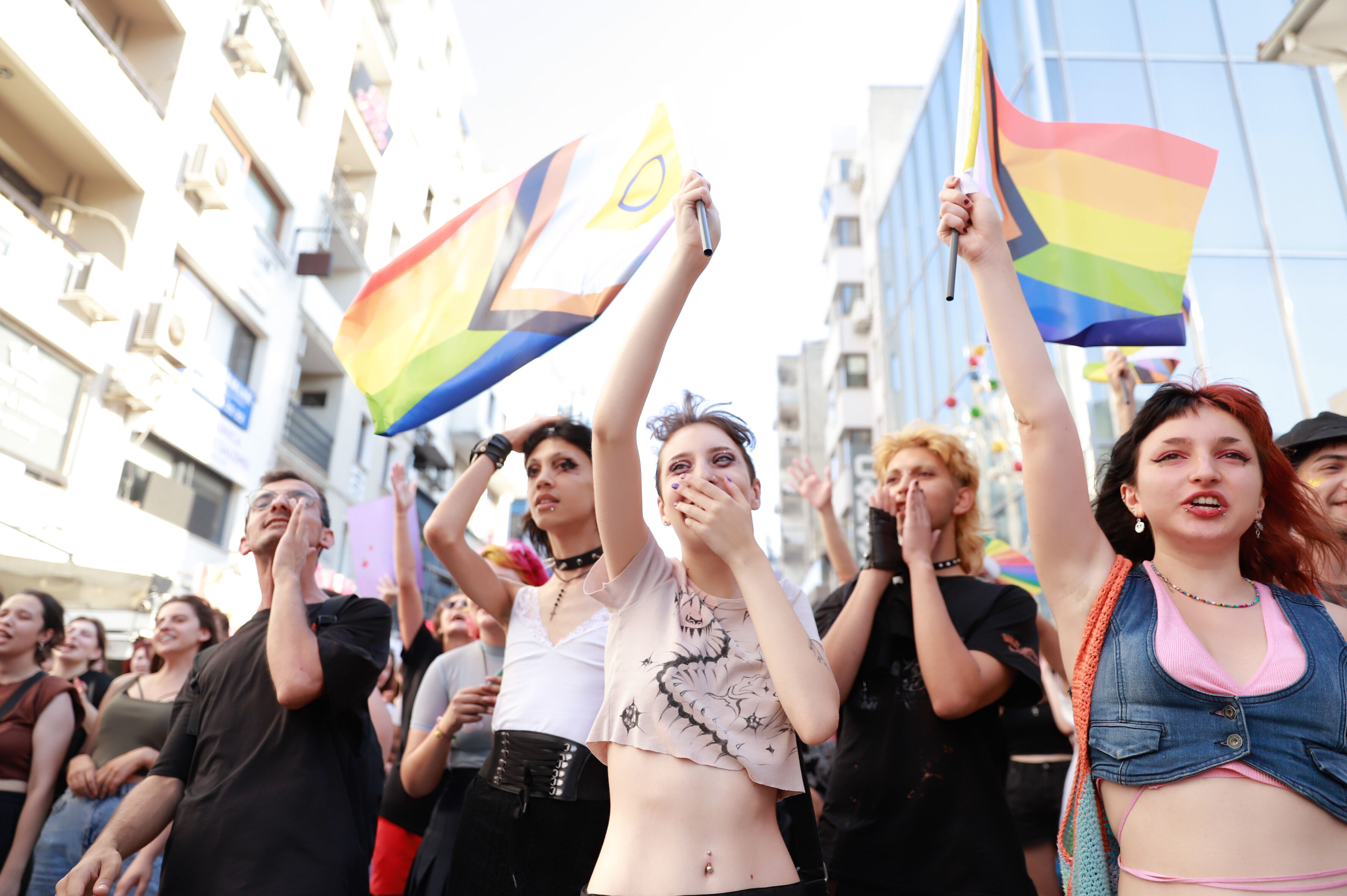 Das Foto zeigt mehrere Personen auf einer Kundgebung. Sie rufen Slogan und halten Regenbogenfahnen in der Hand. Einige lachen.