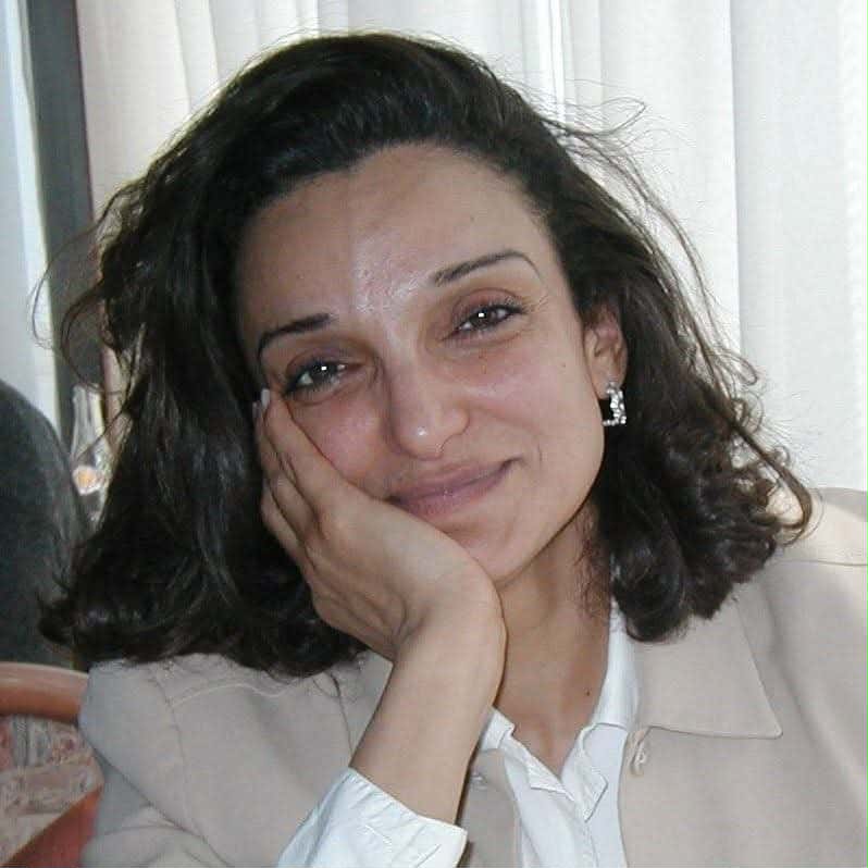 Porträtfoto von Saloua Ghrissa, die ihren Kopf mit ihrer rechten Hand stützt und in die Kamera lächelt.