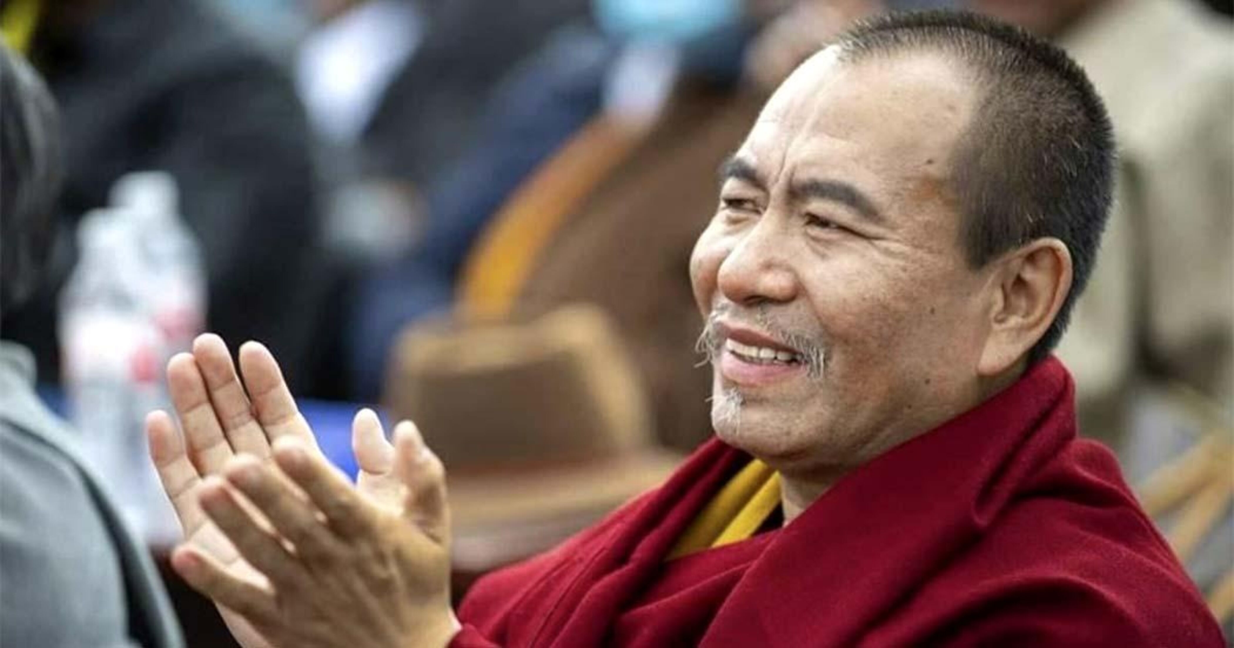 Seitenaufnahme von Choktrul Dorje Ten Rinpoche. Er lächelt und klatscht in die Hände.