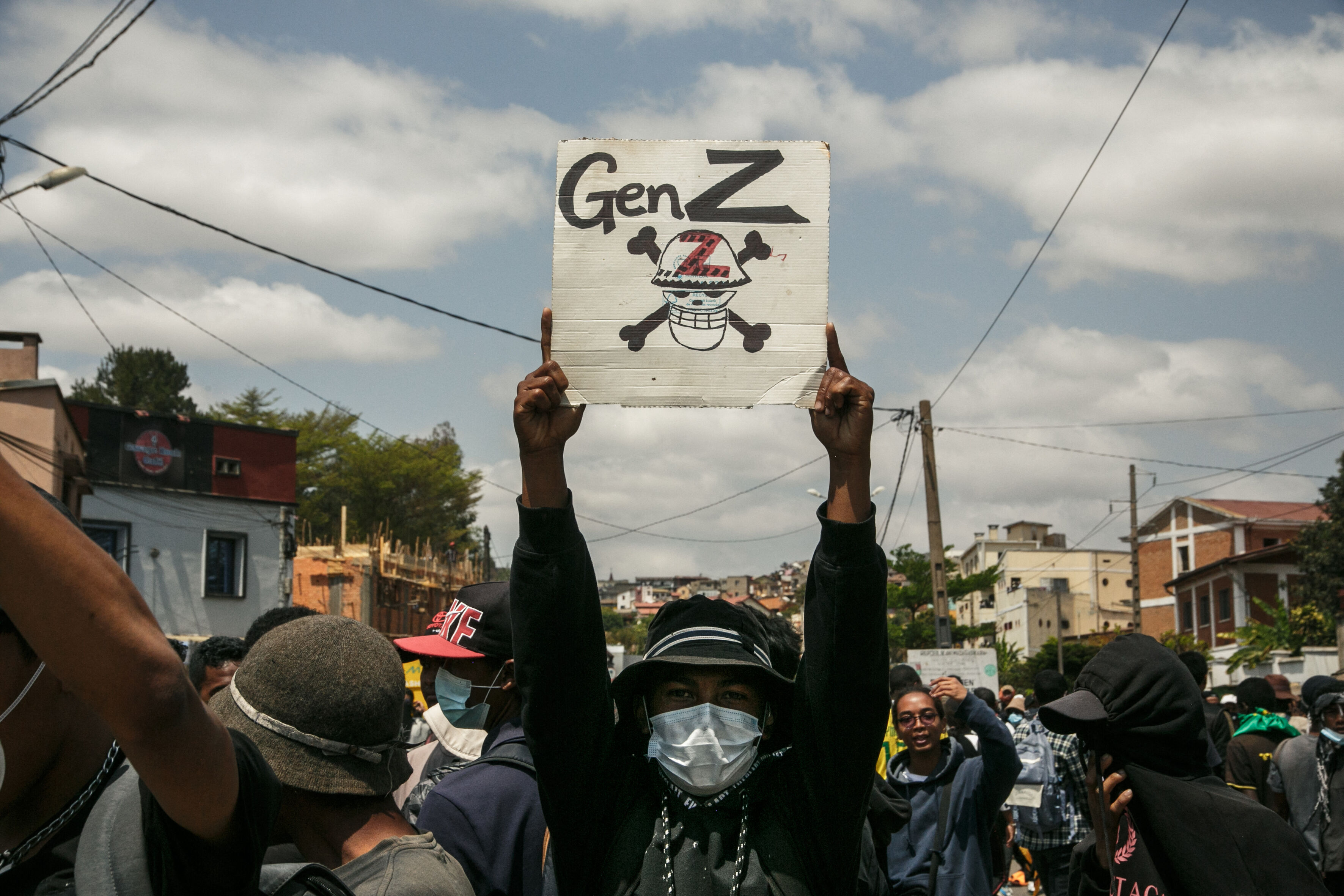 Eine Person mit Mundschutz hält bei einer Demonstration ein Plakat hoch, auf dem ein Totenschädel mit Knochen abgebildet ist. Darüber steht: "Gen Z".