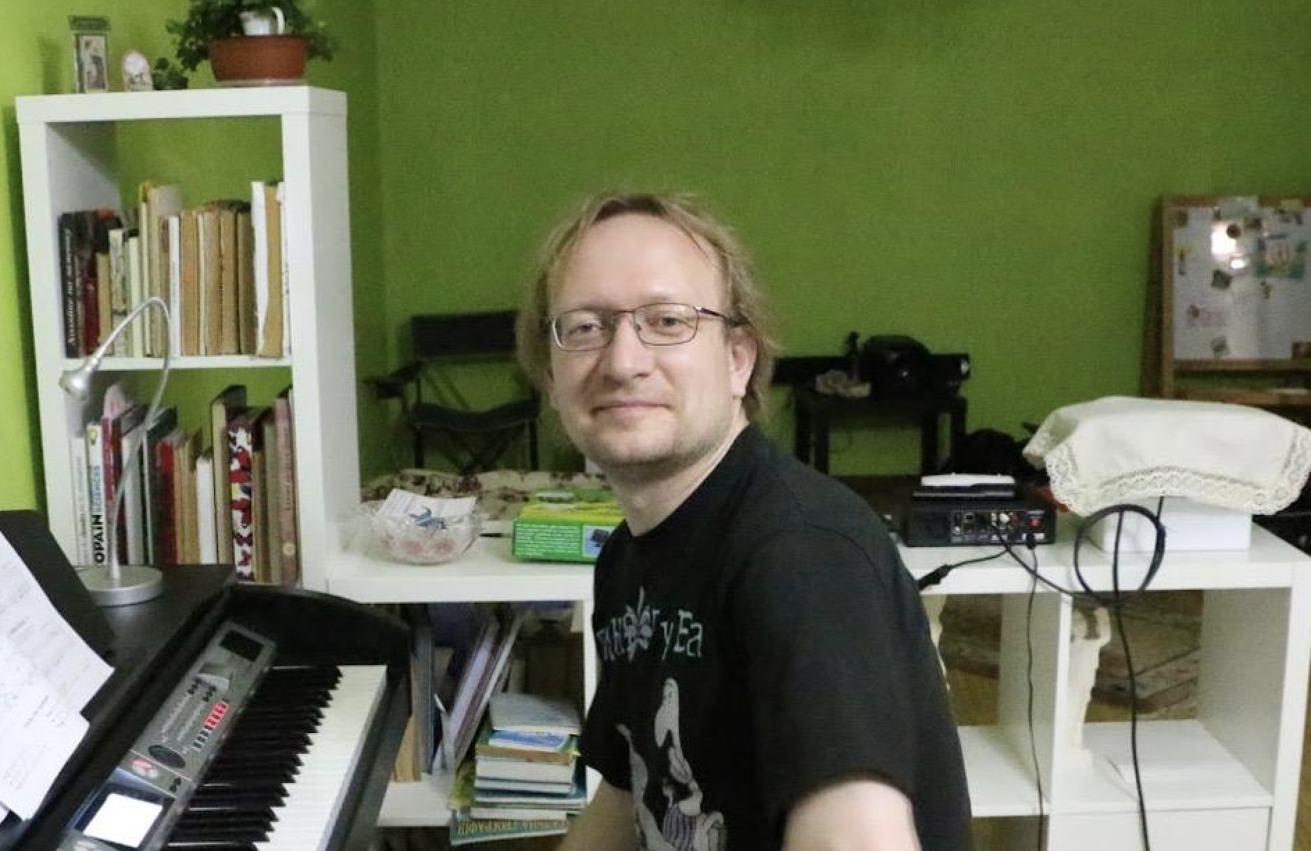 Mikhail Lochtchinin sitzt an einem Keyboad und lächelt in die Kamera. Er trägt eine Brille.