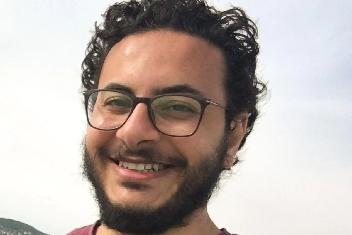 Porträt eines Mannes mit dunklen Locken und Brille, der in die Kamera lächelt.