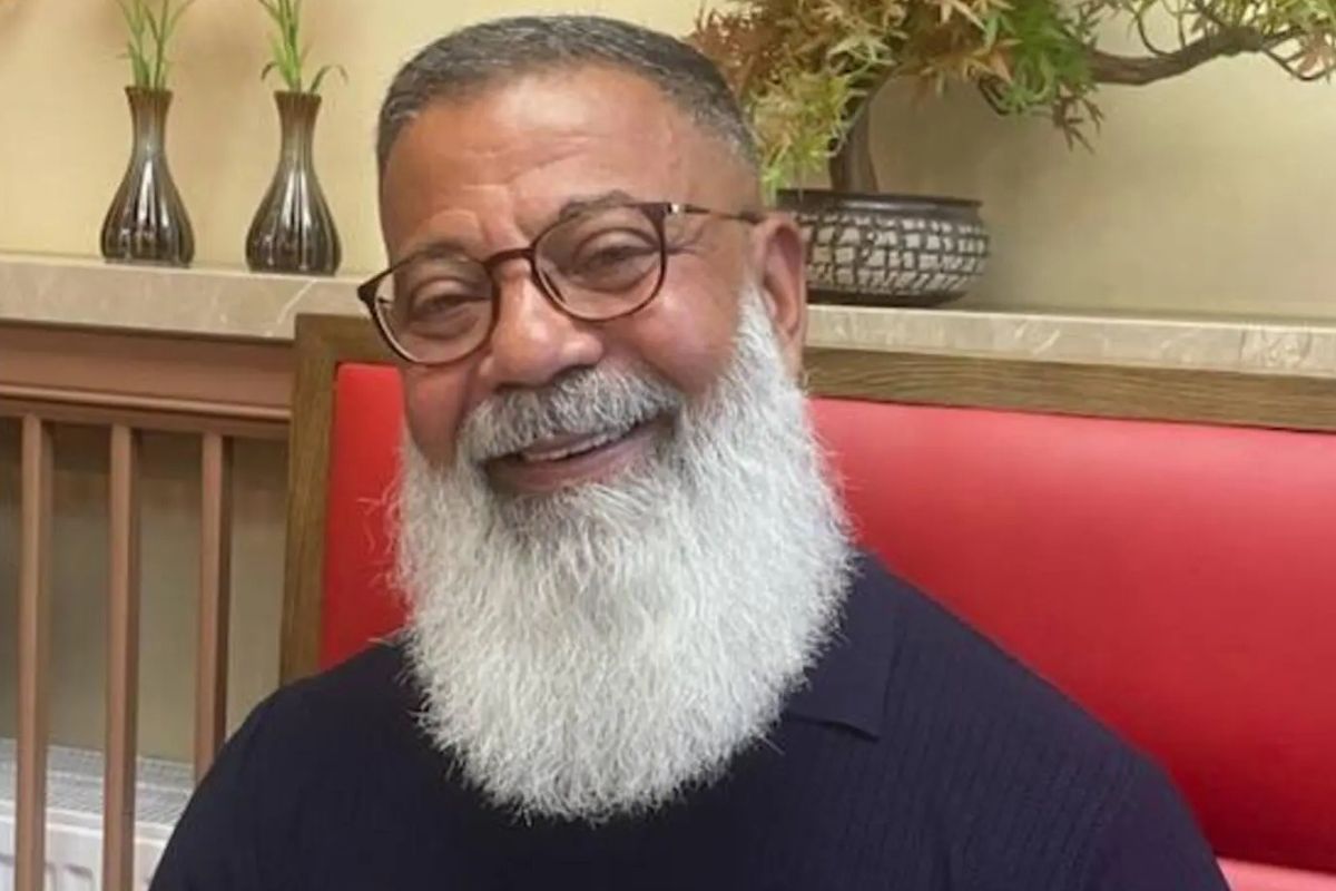 Porträtfoto von Hassan El Sayed, der auf gepolsterten Bank an einem Tisch sitzt. Er hat einen langen Vollbart und trägt Brille und T-Shirt und lächelt in die Kamera.
