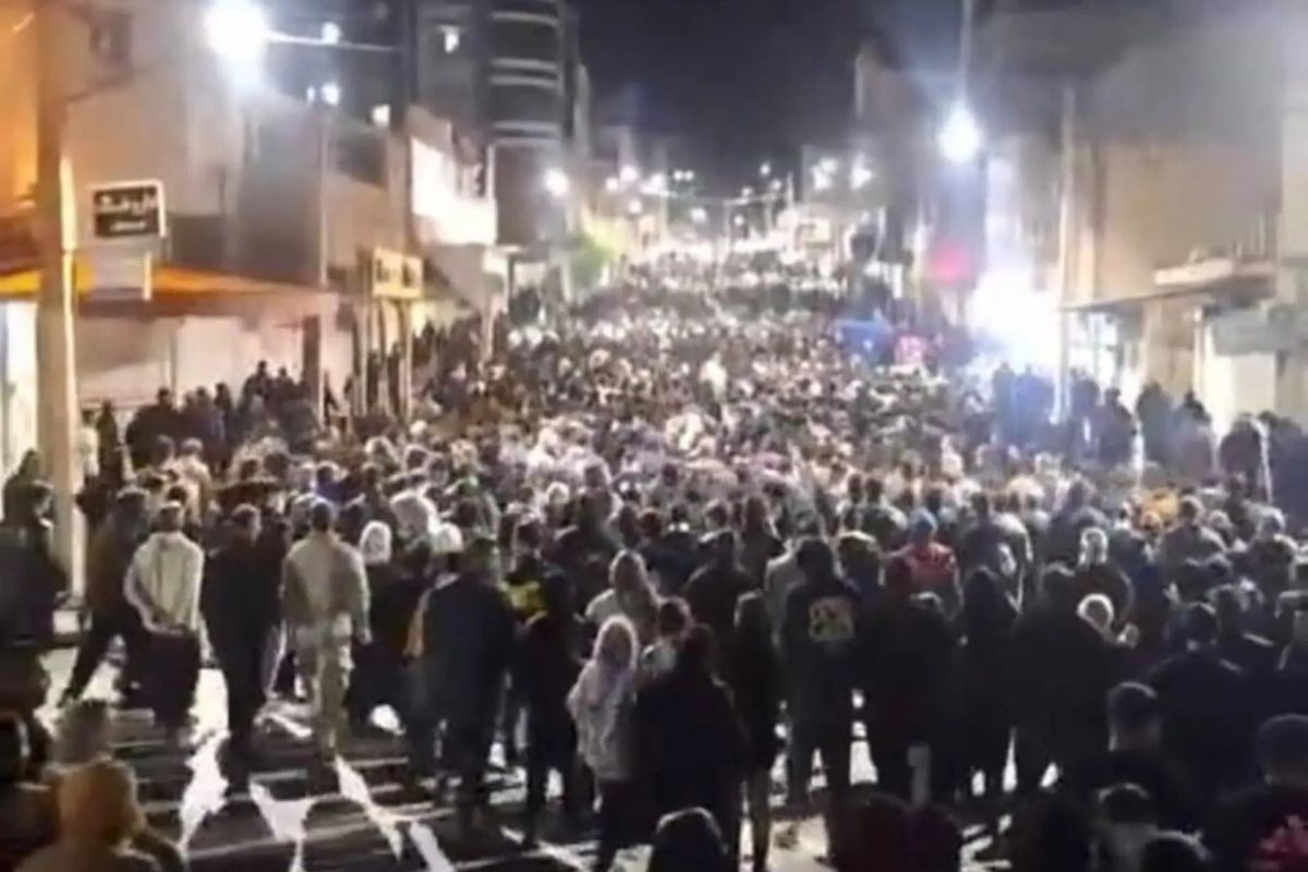Das Foto zeigt einen großen Demonstrationszug, der nachts durch die beleuchtete Straße in einer Stadt zieht.