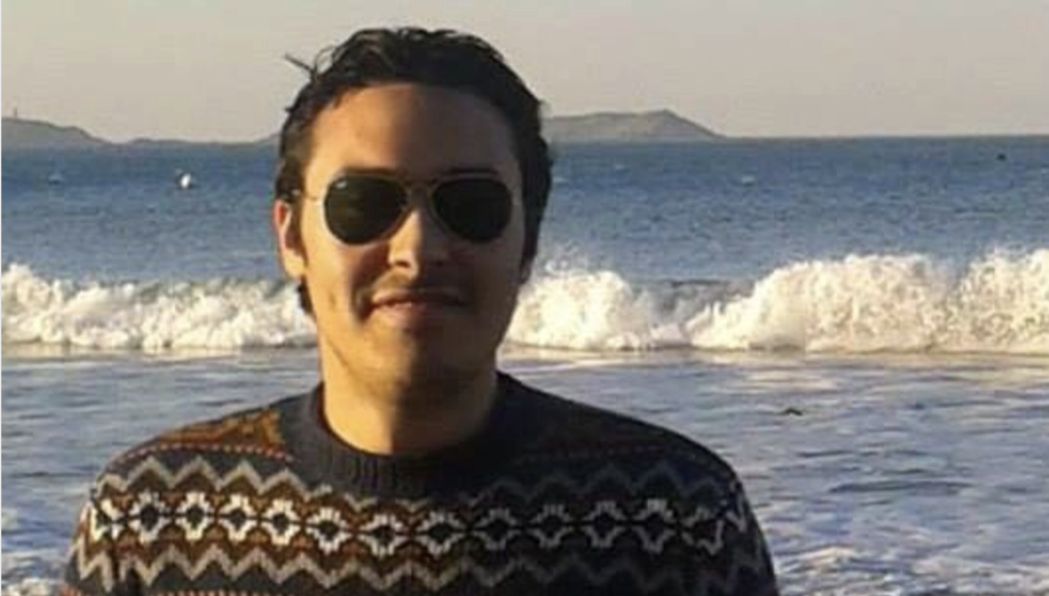 Porträtfoto von Amr Abdelfattah mit dem Meer im Hintergrund. Er trägt eine Sonnenbrille und lächelt in die Kamera.