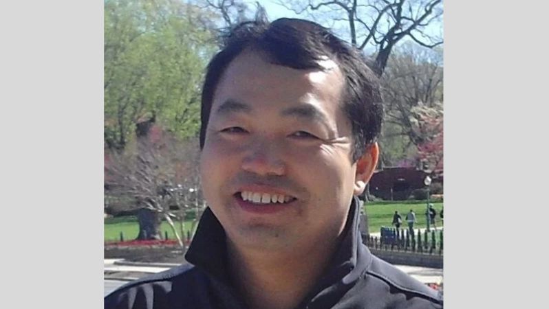 Portraitfoto eines Mannes mittleren Alters, der in einem Park steht und in die Kamera lächelt.