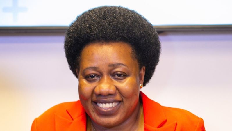 Dr. Sarah Bireete sitzt in einem Stuhl und lächelt in die Kamera.