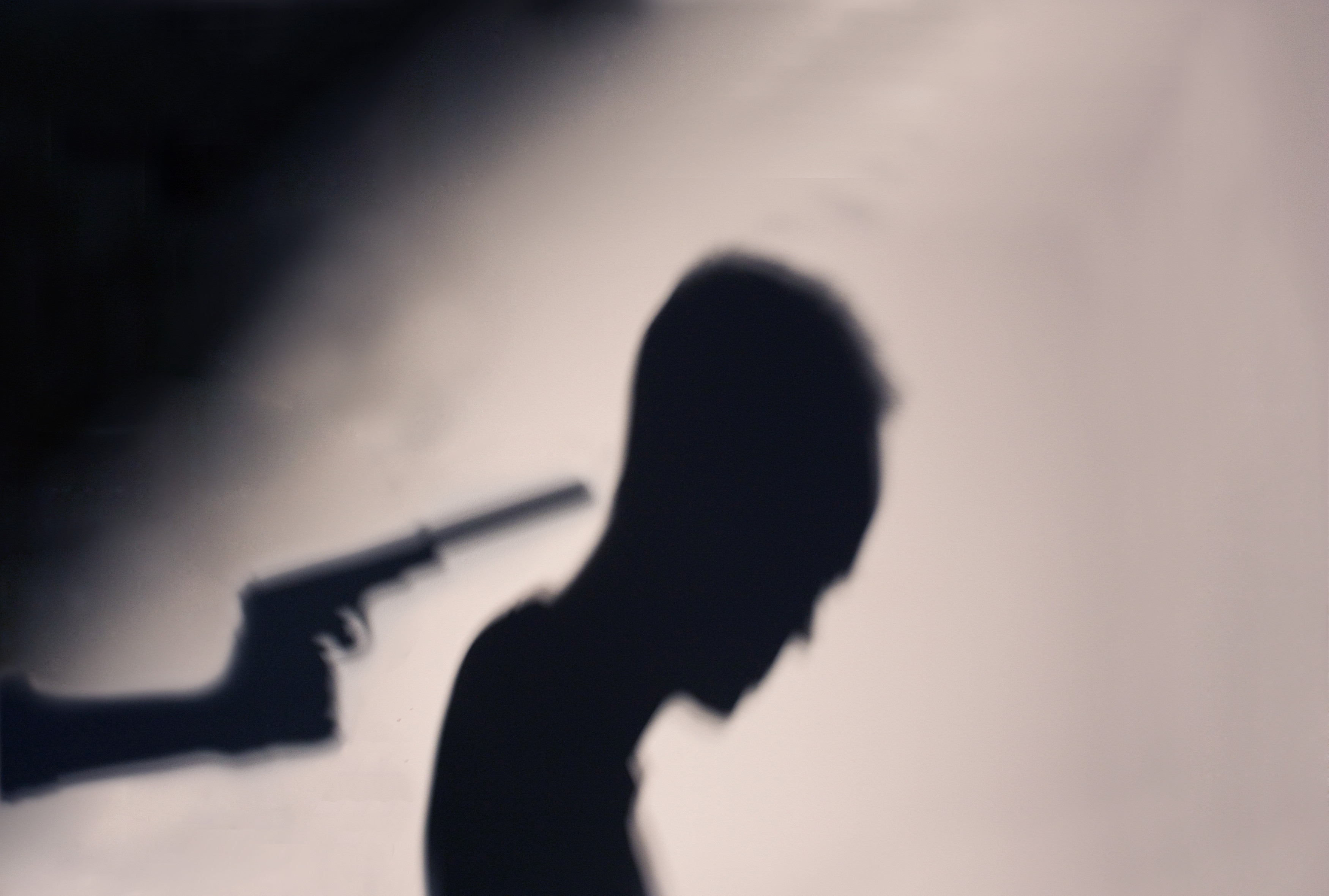 Silhouette eines Mannes, dem eine Pistole an den Hinterkopf gehalten wird