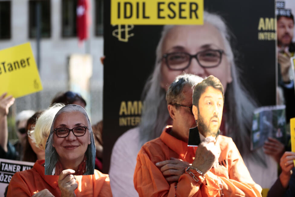 Eine Gruppe von Amnesty-Aktivistinnen und Aktivisten steht vor der Berliner Mauer, hält Banner und Schilder vor der türkischen Botschaft hoch