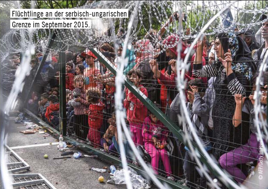 Geflüchtete Menschen stehen an einem Grenzzaun