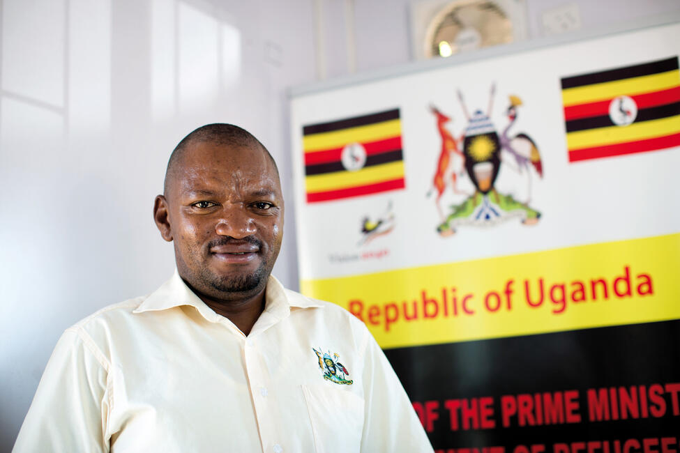 Porträtbild von einem Mann, hinter dem sich ein Banner der Republik Uganda befindet