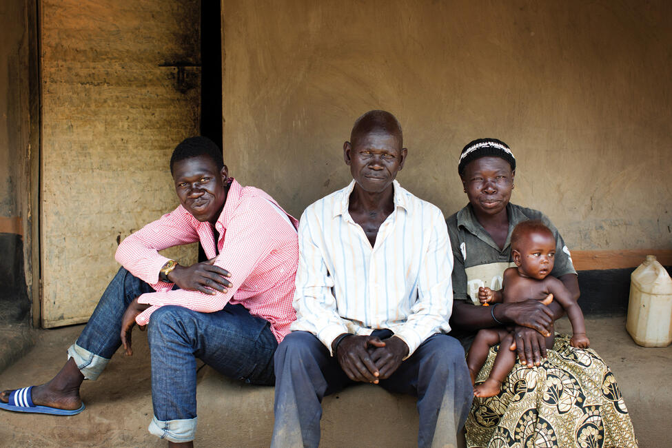 Eine Vierköpfige-Familie mit Kleinkind sitzt vor einer kargen Wand