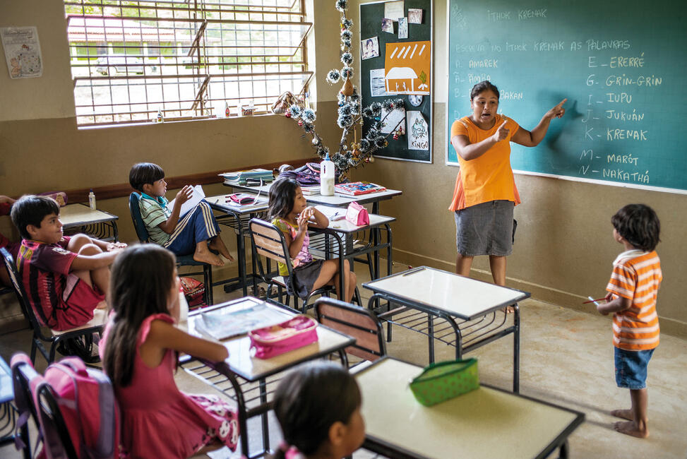 Krenak-Kinder sitzen in einem Klassenzimmer, während die Lehrerin an der Tafel Vokabeln erklärt.