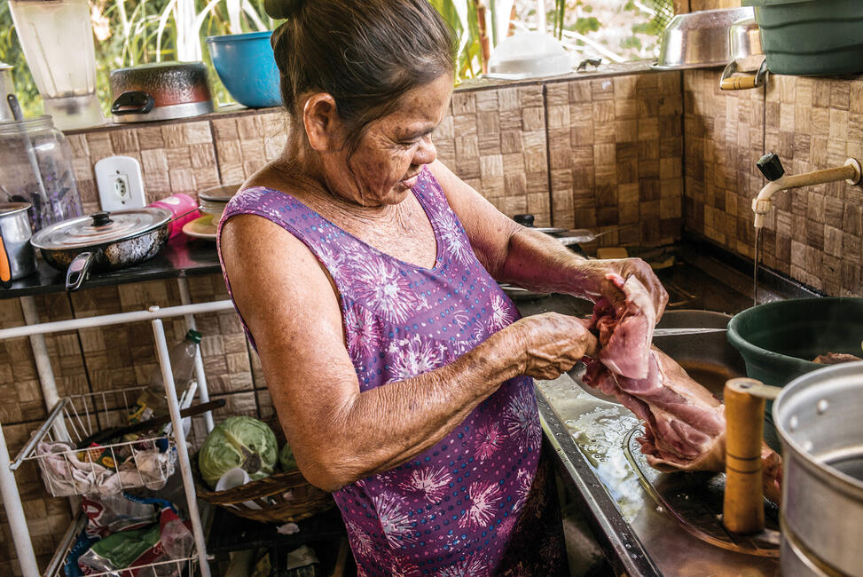 Dejanira Krenak steht in der Küche und bereitet ein Stück rohes Fleisch vor.