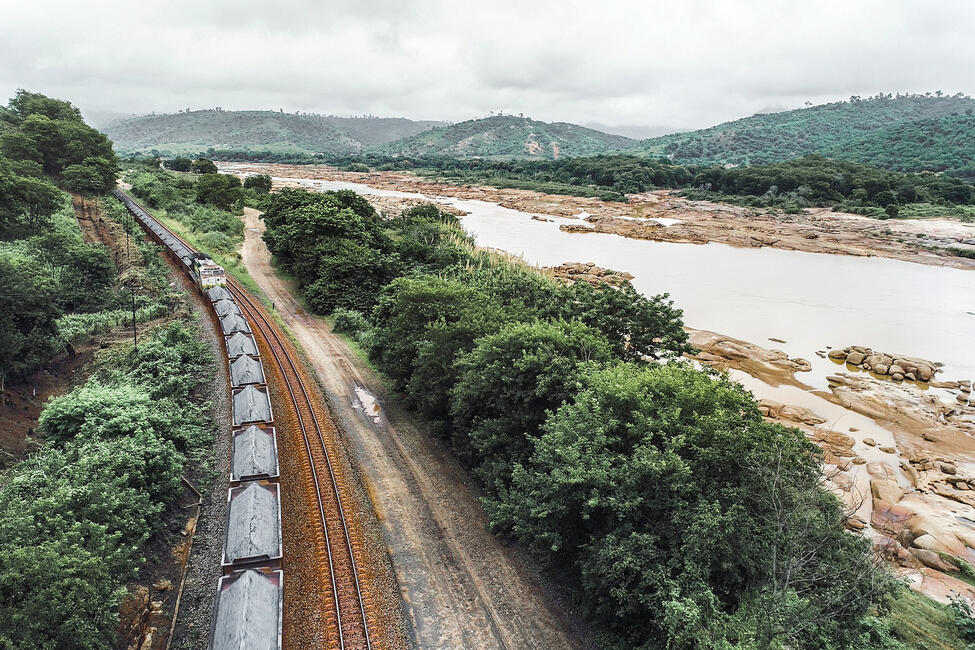 Auf der linken Seite des Rio Doce fährt ein Güterzug auf Gleisen entlang