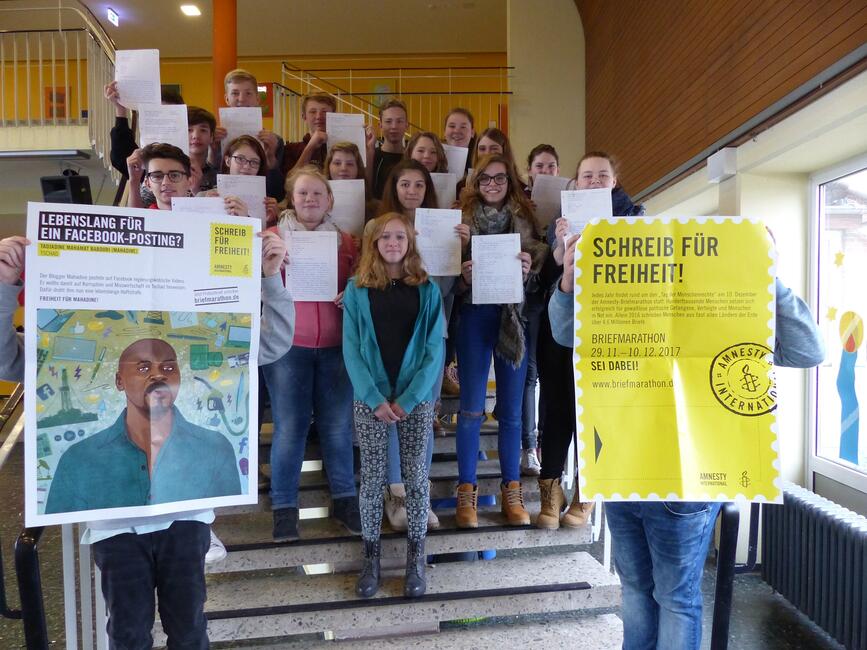 Eine Gruppe aus Schülerinnen und Schülern steht auf einer Treppe, zwei Plakate über den Briefmarathon 2017 werden hochgehalten