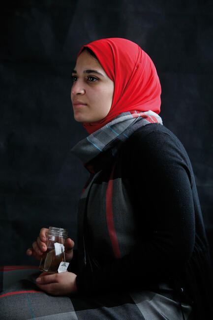 Junge Frau mit rotem Kopftuch hält ein Glas mit Tee in der Hand