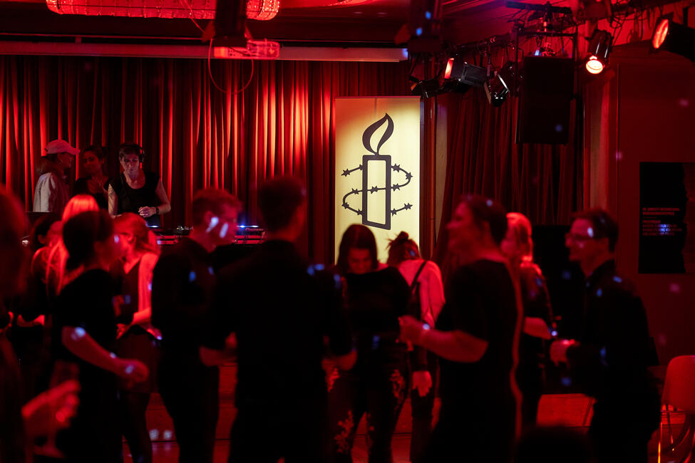 Menschen tanzen in einem Raum mit rotem Licht, im Hintergrund legt eine DJane auf