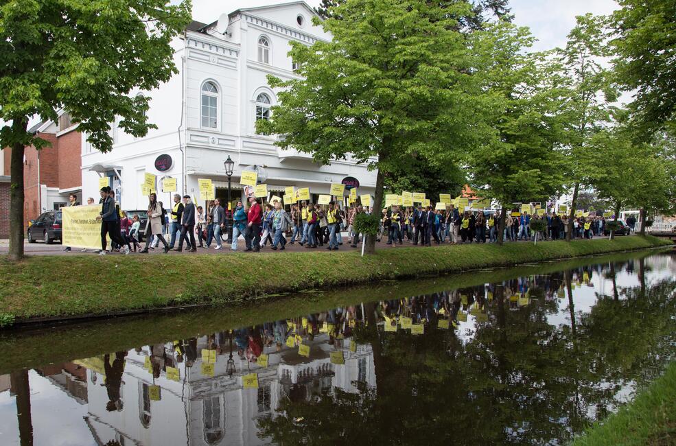 Ein langer Demonstrationszug von vielen Menschen, die viele gelbe Transparente tragen, an einem Kanal in der Stadt