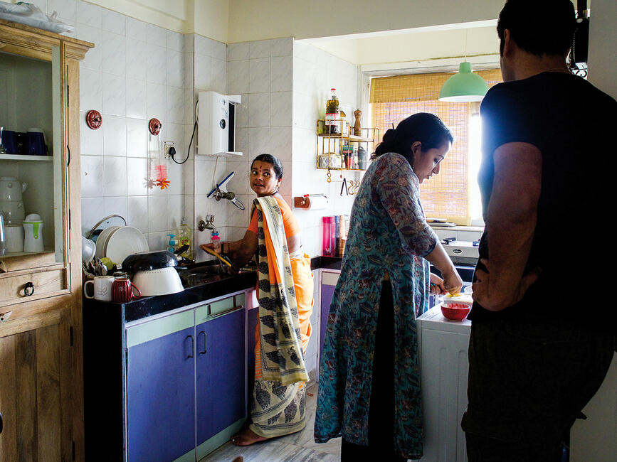 Zwei Frauen arbeiten in der Küche, am Bildrand steht ein Mann und schaut zu