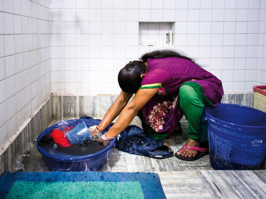 Eine Frau hockt vor einer Plastikwanne und wäscht Kleidung