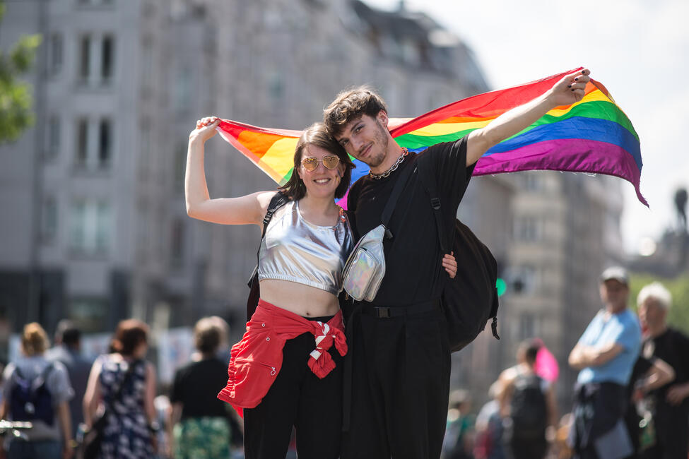 Zwei Personen halten eine Regenbogenflagge und umarmen sich