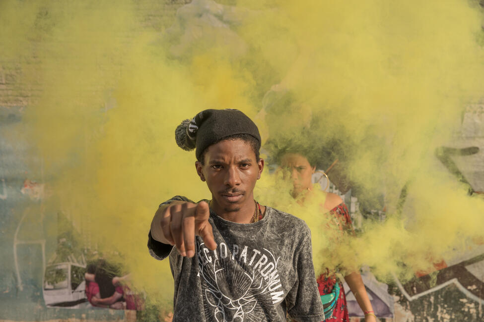 Ein junger Demonstrierender umhüllt von gelben Nebel schaut in die Kamera und zeigt mit einem Finger auf die Kamera.