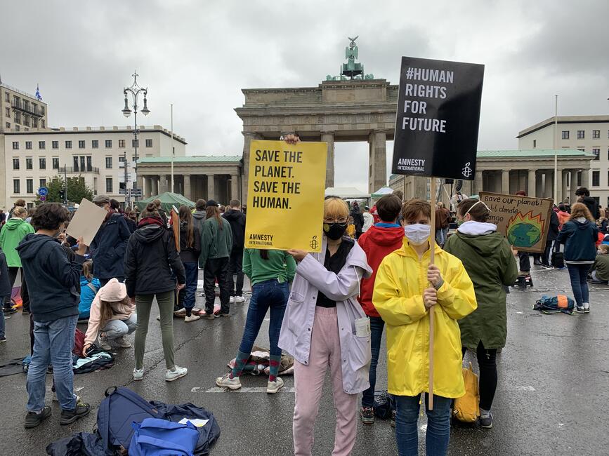 Demonstrierende vor dem Brandenburger Tor in Berlin, es regnet, die Schilder haben Aufschriften wie "#Human Rights for Future"