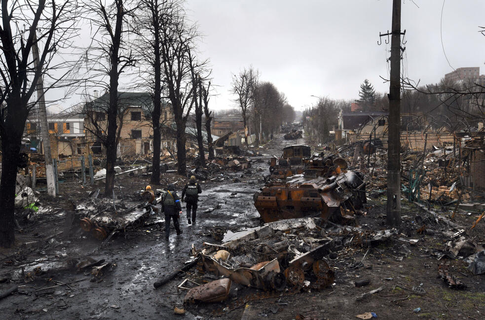 Das Bild zeigt eine Straße mit zerstörten Panzern, Resten von Fahrzeugen und Gebäuden